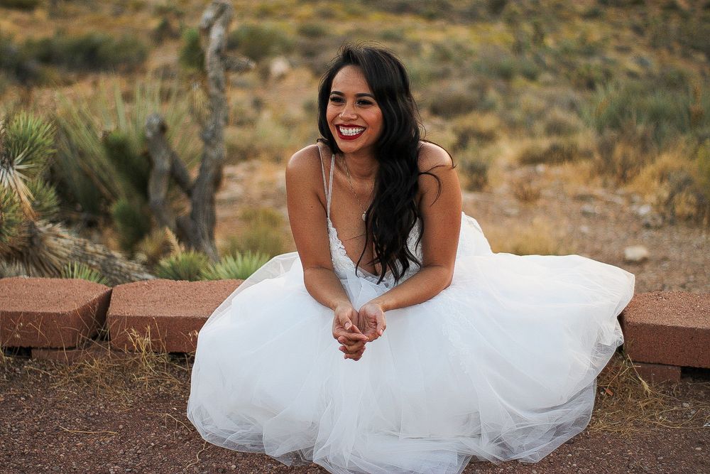 Radiant bride in white tulle gown sitting outdoors laughing in desert garden setting.