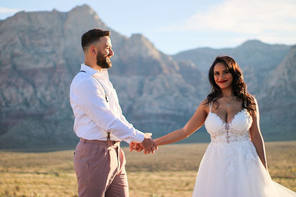 Bride and groom holding hands walking through desert with stunning Red Rock Canyon mountains.