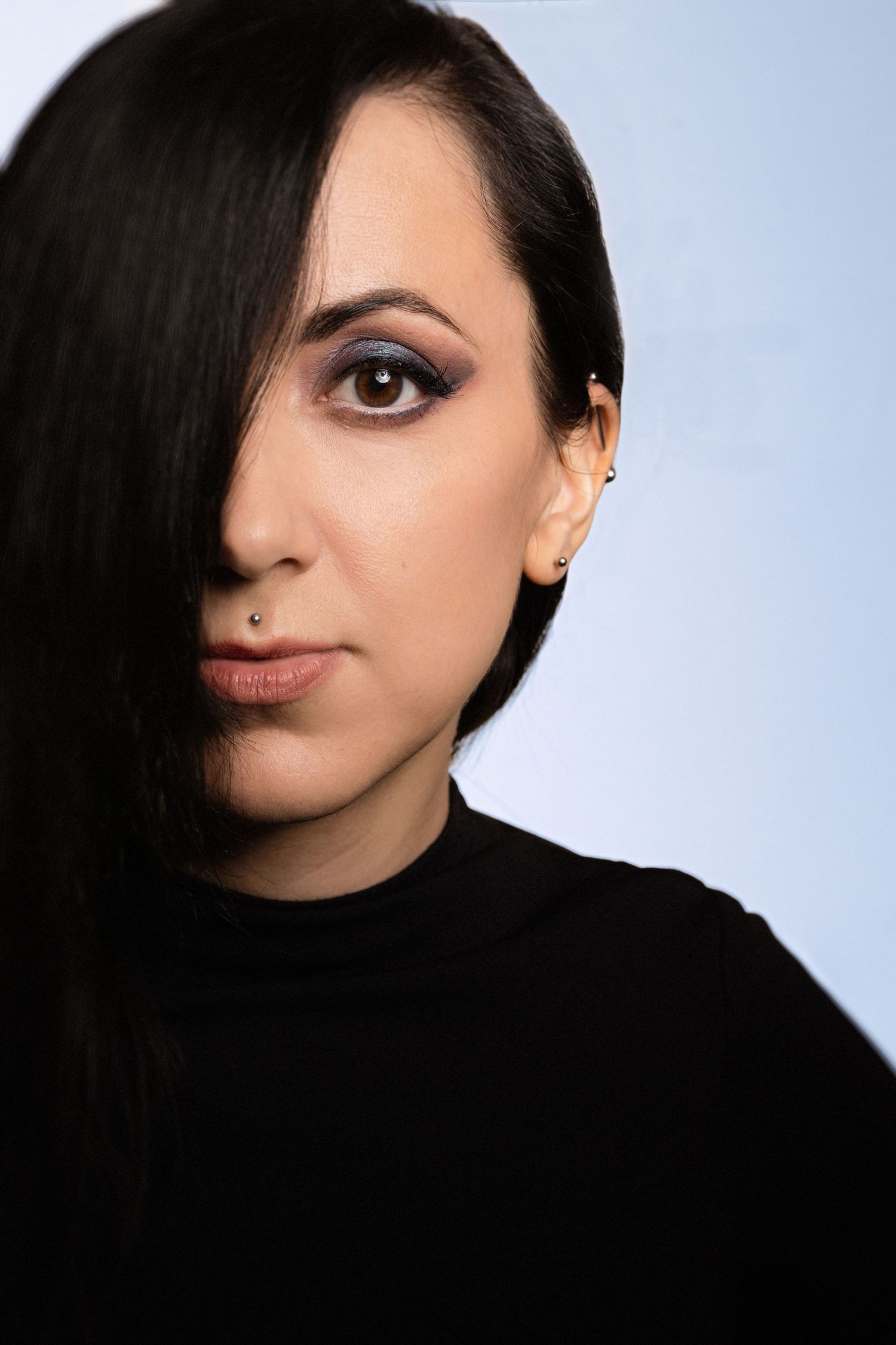 Portrait of someone in a black top against a light background showcasing dramatic eye makeup and lighting.
