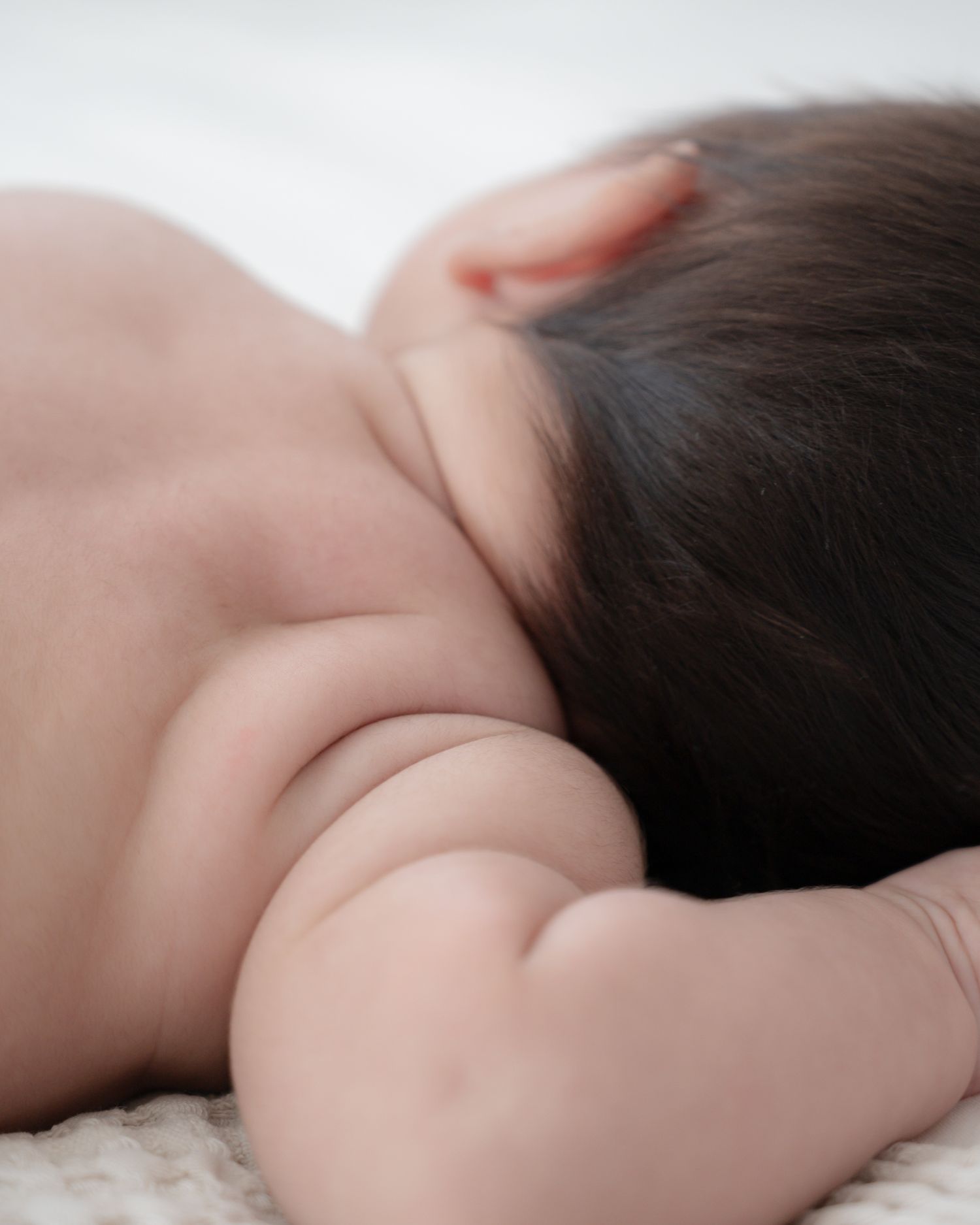 Peaceful sleeping baby with dark hair resting on soft white surface.