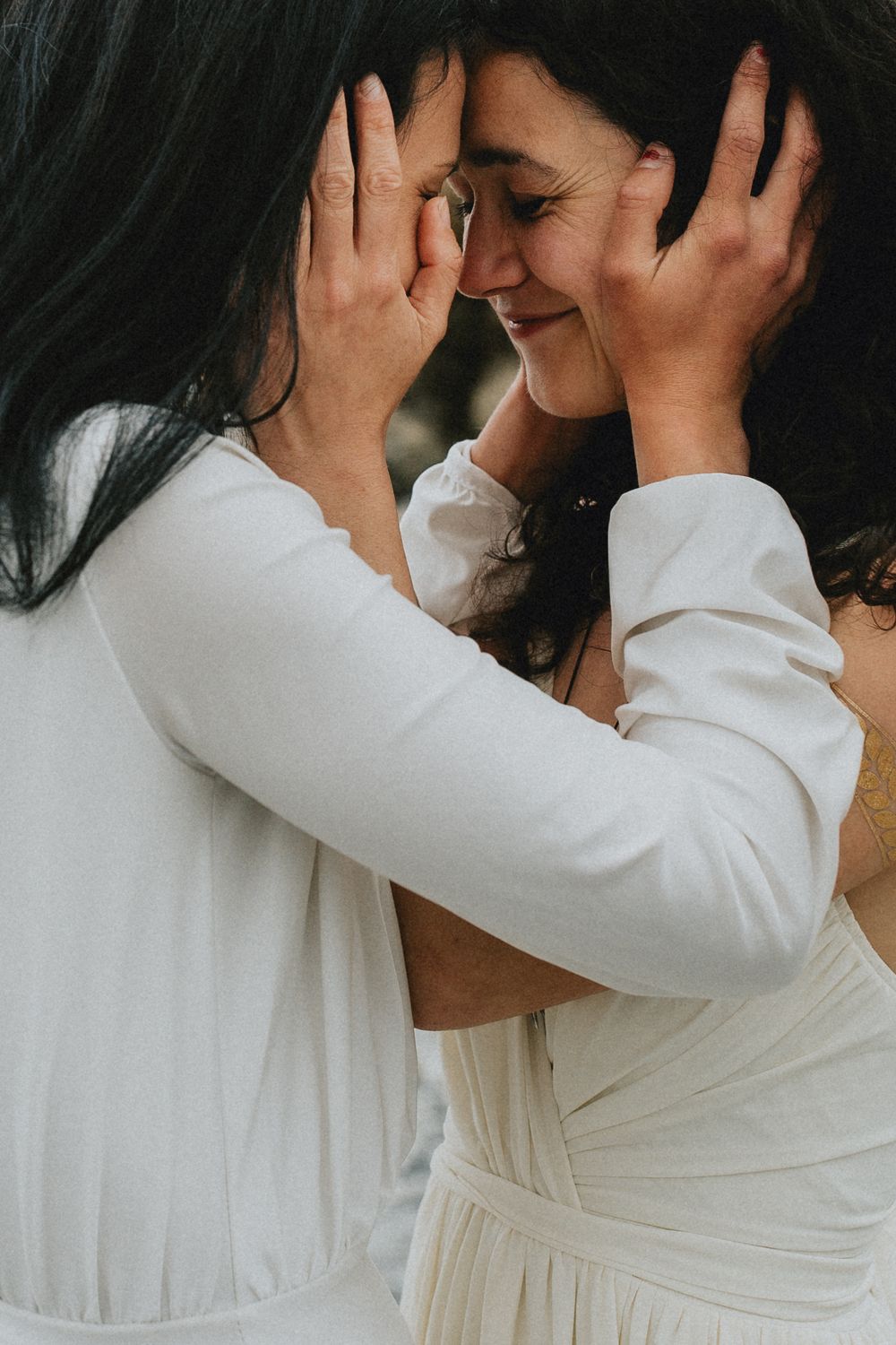Close-up intimate moment between two people wearing white against natural backdrop.