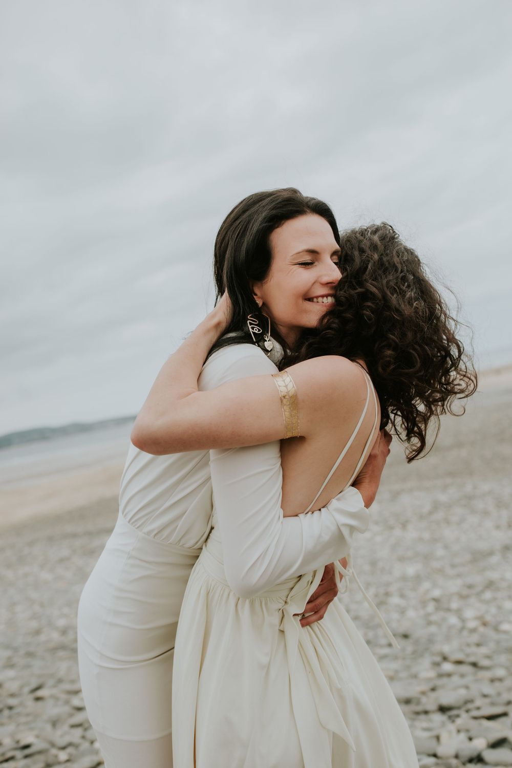 Joyful embrace shared between two people in white dresses on a beach.