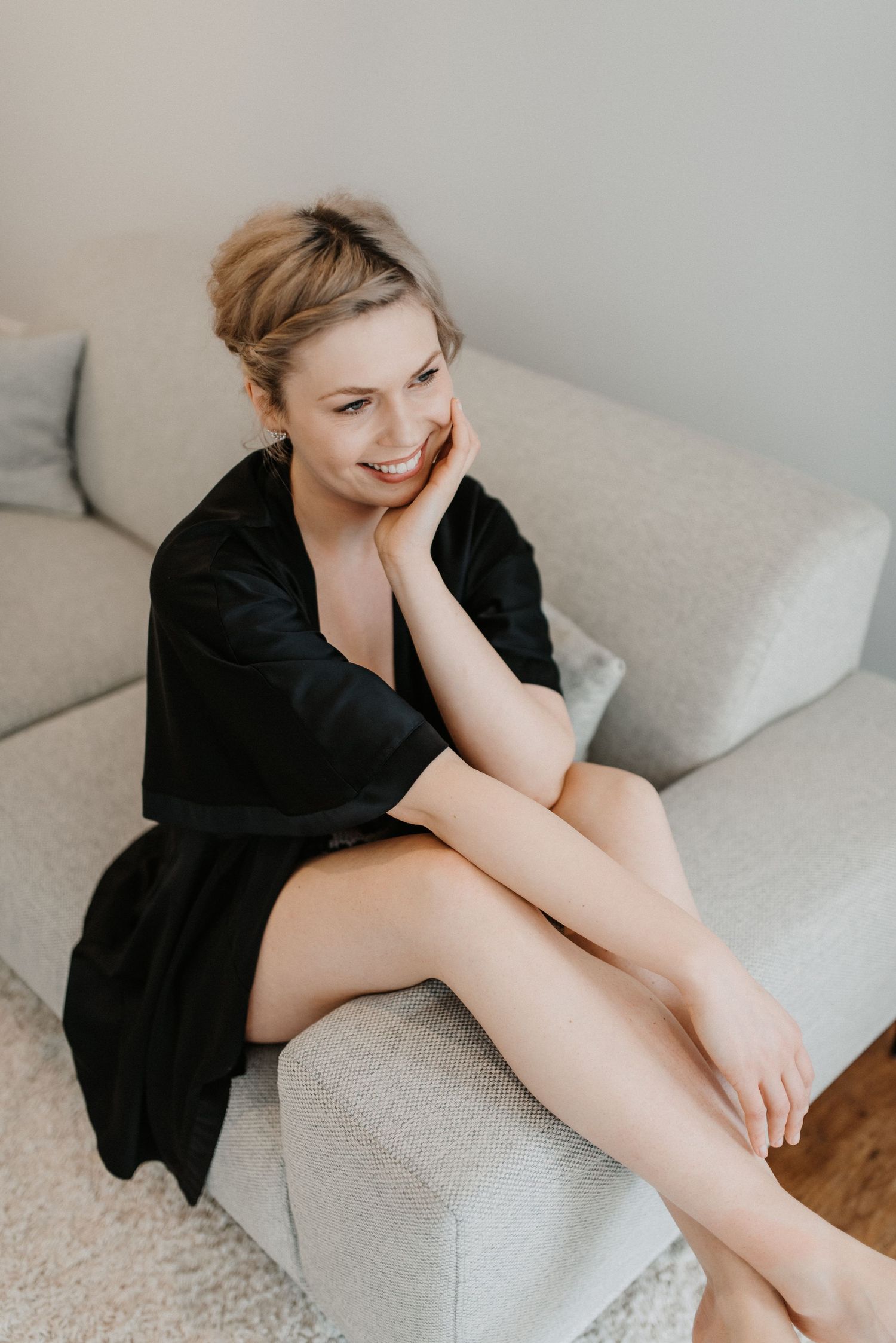 A candid lifestyle portrait of a woman relaxing on a grey couch in a black robe.