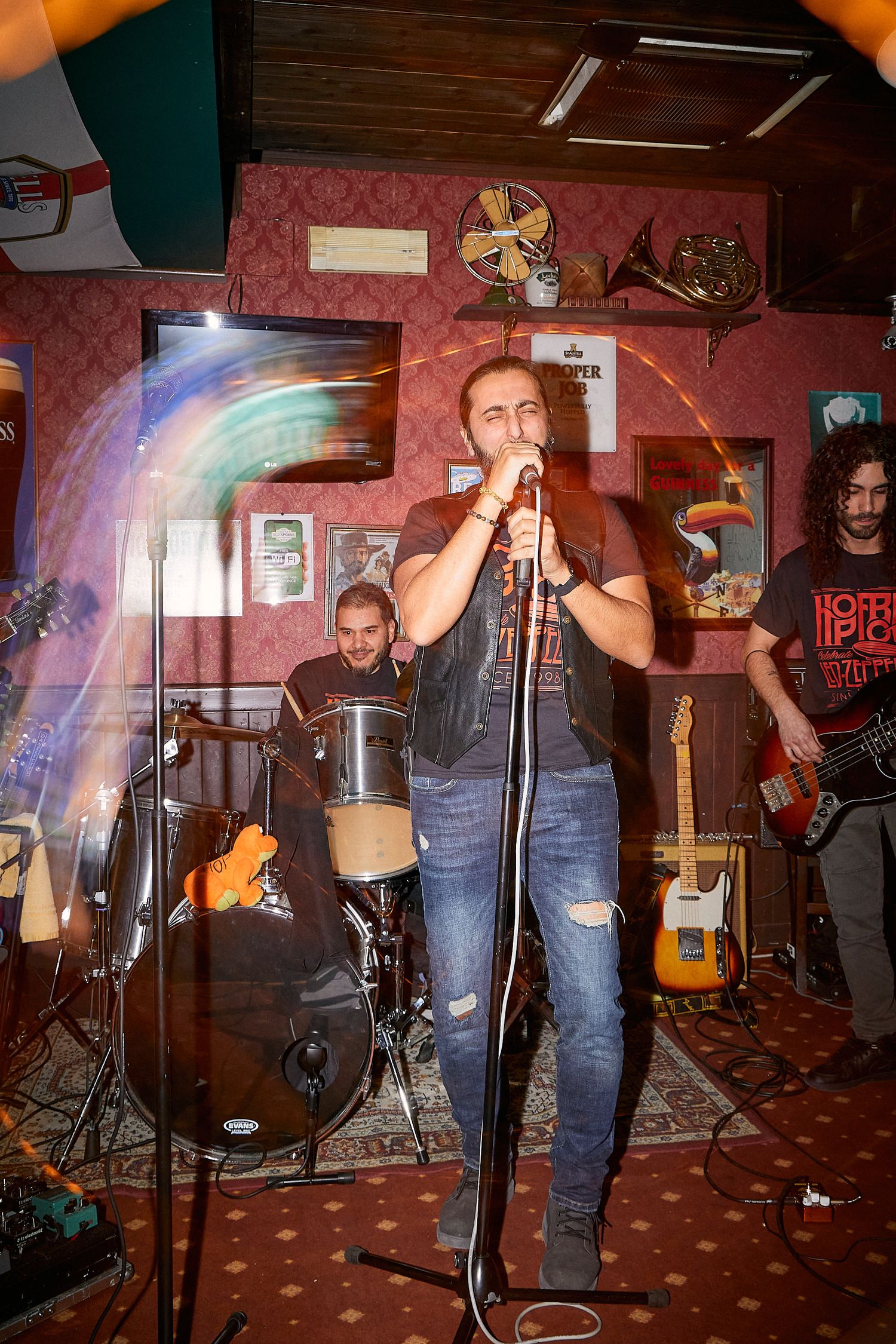 Live band performing on small stage with colorful lighting effects in intimate venue setting.
