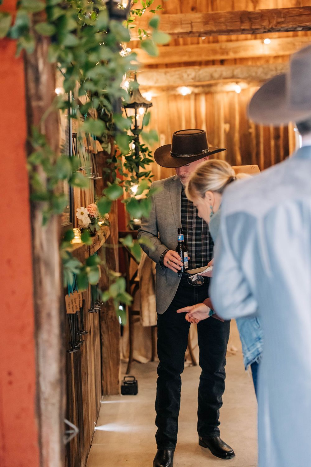 A rustic barn venue decorated for a wedding with string lights and greenery along wooden beams and posts.