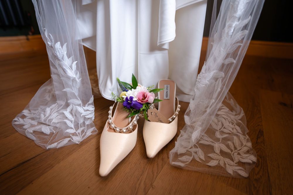 The shoes of the Bride-to-be sat under her dress along with the flowers of the groom gently lay on top.