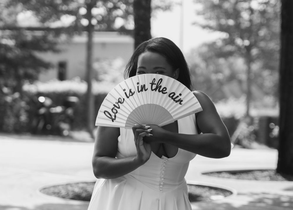 A bride using a fan that reads, Love is in the air, to cool herself down on her wedding day in zürich.