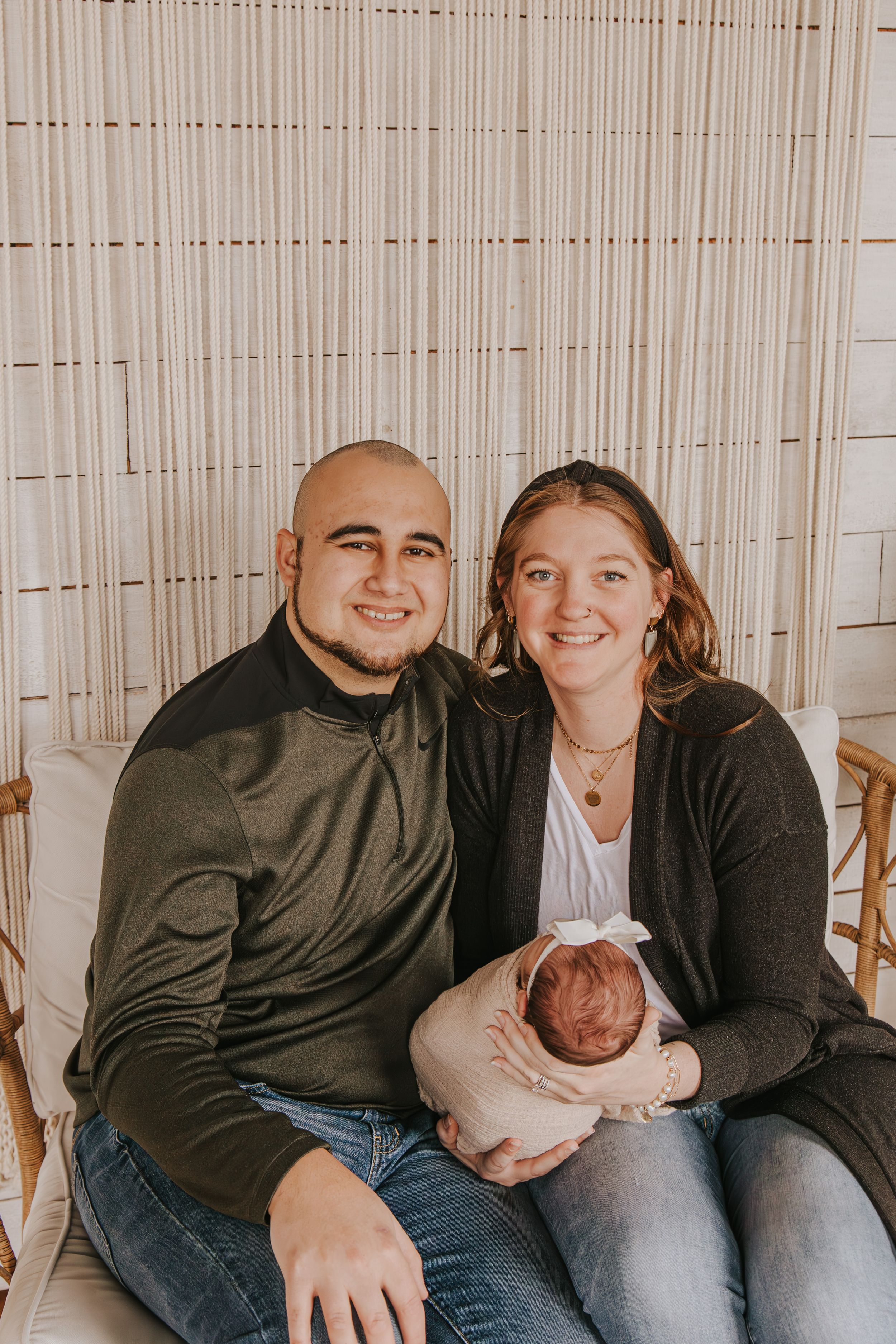Family sitting together on wooden chairs against beige curtain backdrop.