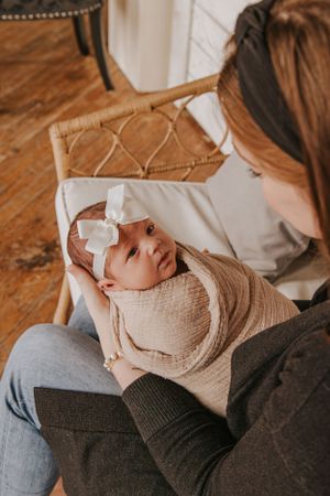 Close-up view of baby wrapped in beige blanket being held on couch.