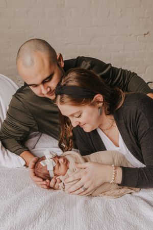 Parents sharing gentle moments with newborn baby on white textured bedding.