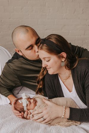 Parents lying on bed sharing intimate moments with their newborn.