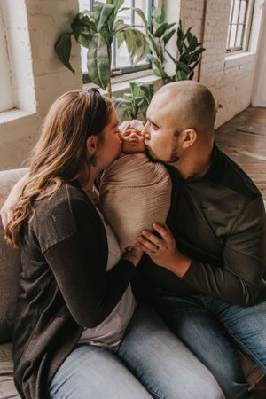 Parents cuddling with their swaddled newborn in cozy indoor setting.