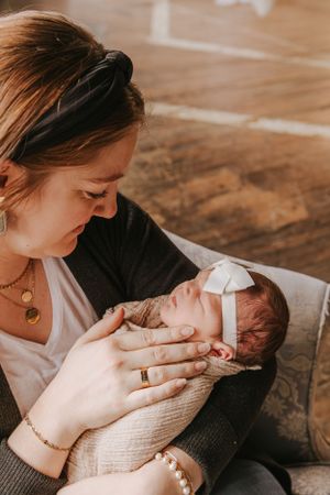 Parent tenderly holding and feeding newborn baby wrapped in light colored swaddle.