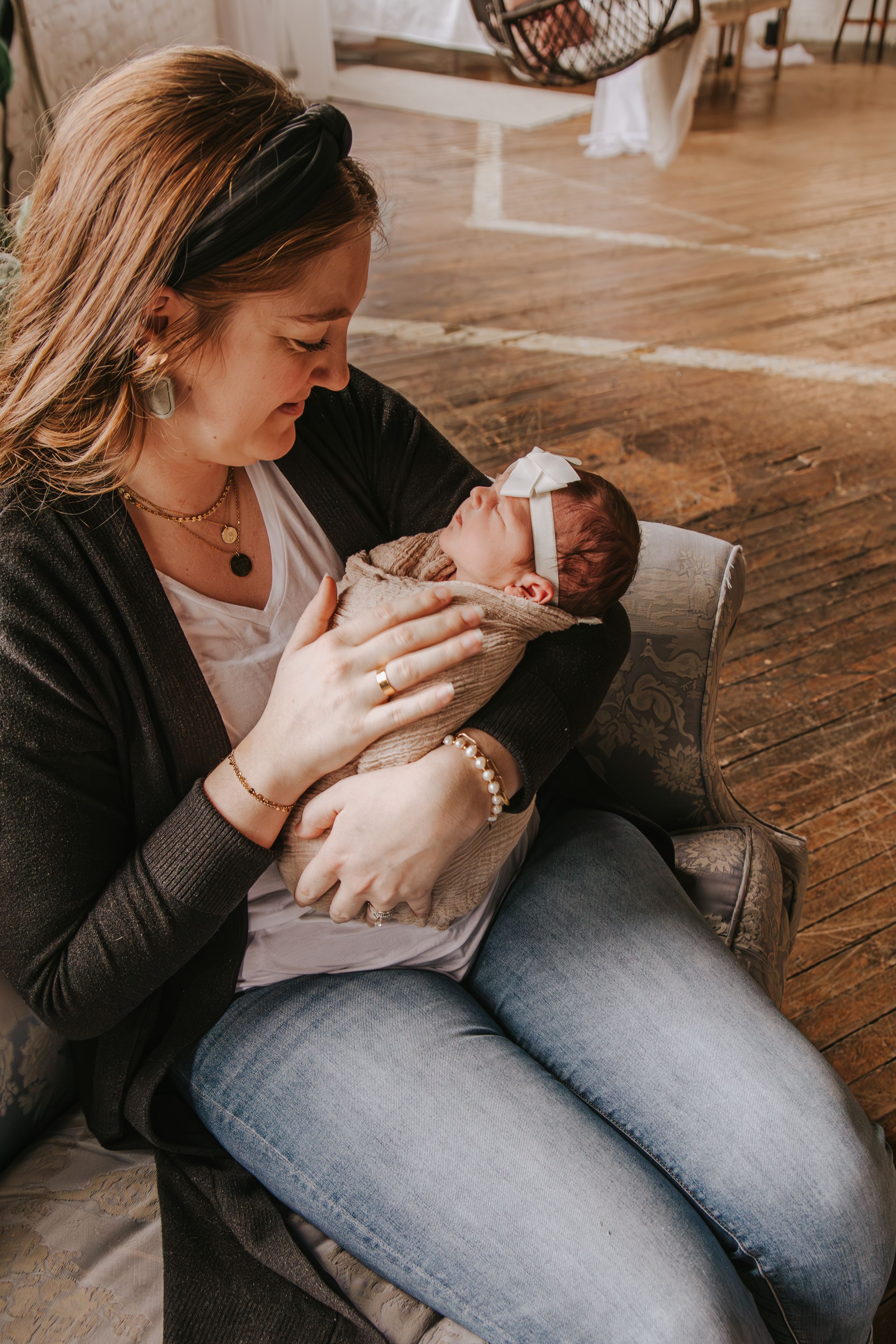 Parent cradling and feeding newborn baby on wooden floor in natural light.