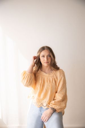 Portrait in a peachy blouse and jeans against white backdrop with soft natural lighting.