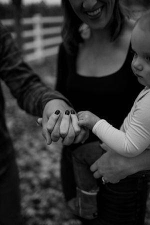Close up of hands holding together in a tender moment against a blurred outdoor background.