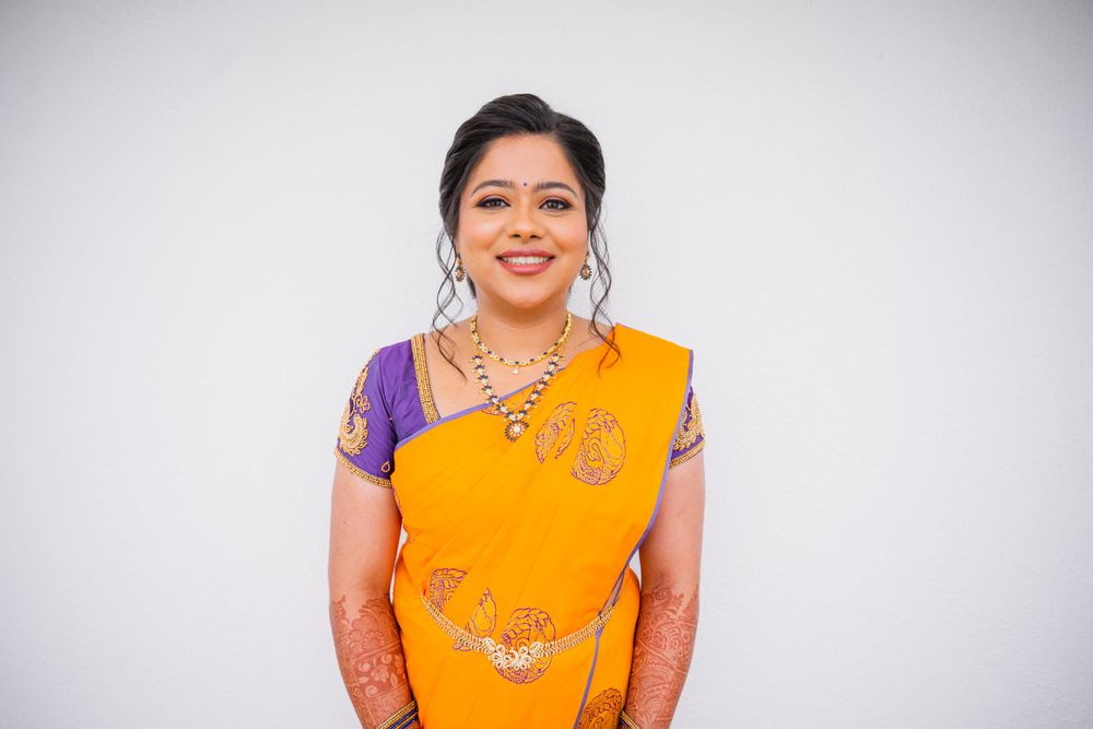 Woman in bright yellow and purple traditional Indian sari smiles against white background.