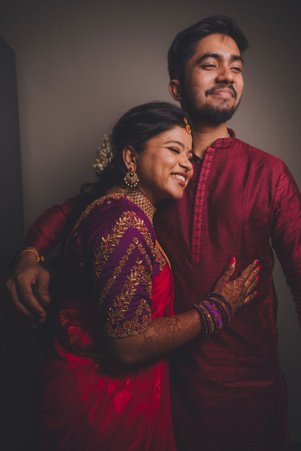 Couple in red and maroon Indian formal wear share joyful moment together.