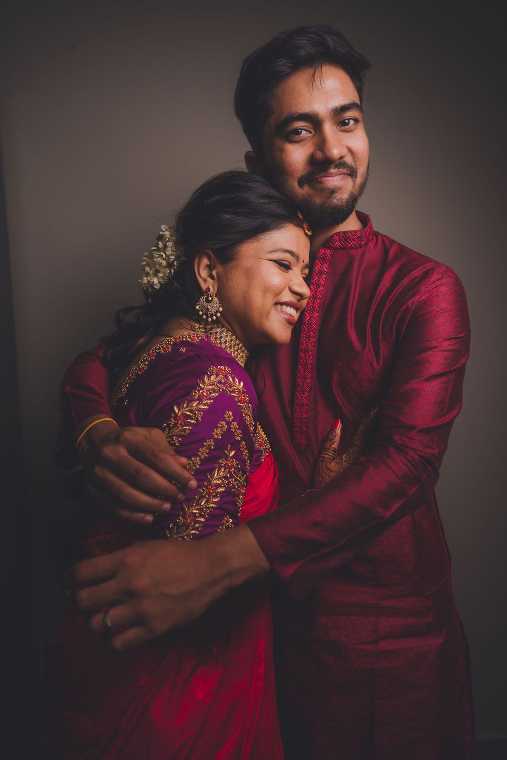 Intimate portrait of couple in traditional Indian attire against dark background.