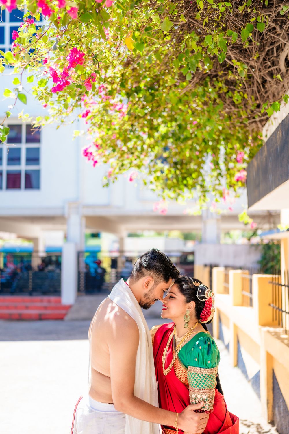 A romantic couple in traditional South Indian wedding attire embracing under pink bougainvillea flowers.