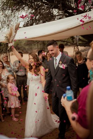 A wedding celebration with flower petals being thrown as the couple walks under a white canopy.