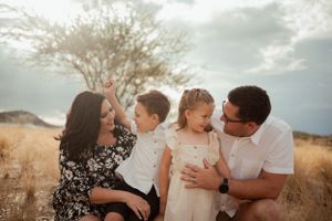 Family sitting together in golden field with mountains in background.