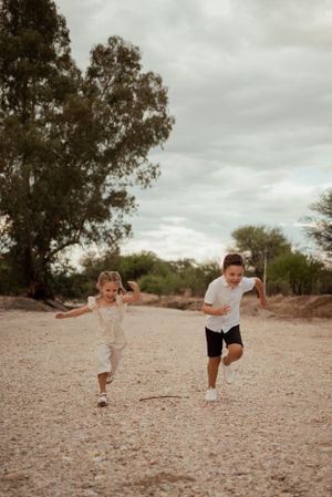 Two children running playfully on desert path under cloudy sky.