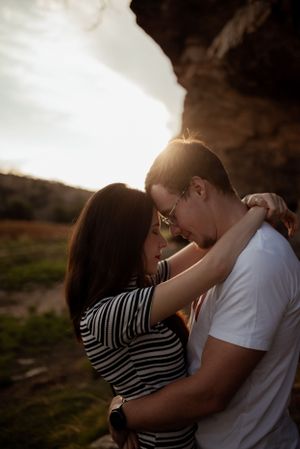 A tender embrace captured during golden hour beneath a rocky overhang.