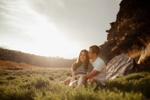 A couple sitting together under a cliff during sunset in a grassy field.