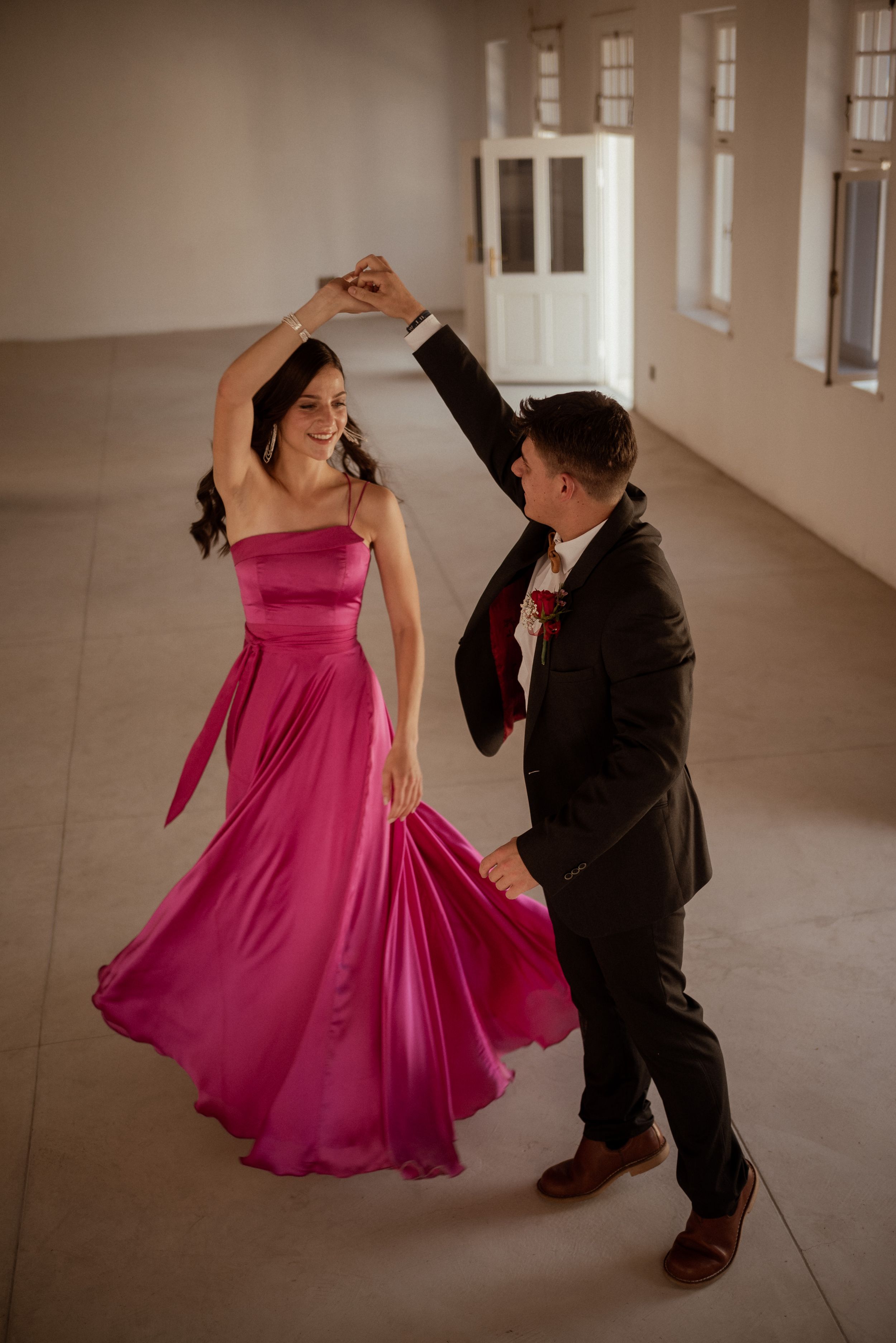 A couple dancing together, with the woman wearing a flowing magenta gown in an elegant indoor space.