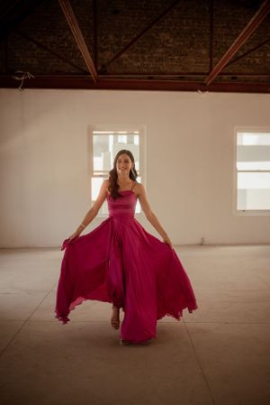 A woman in a vibrant magenta gown twirling in an empty room with natural light.