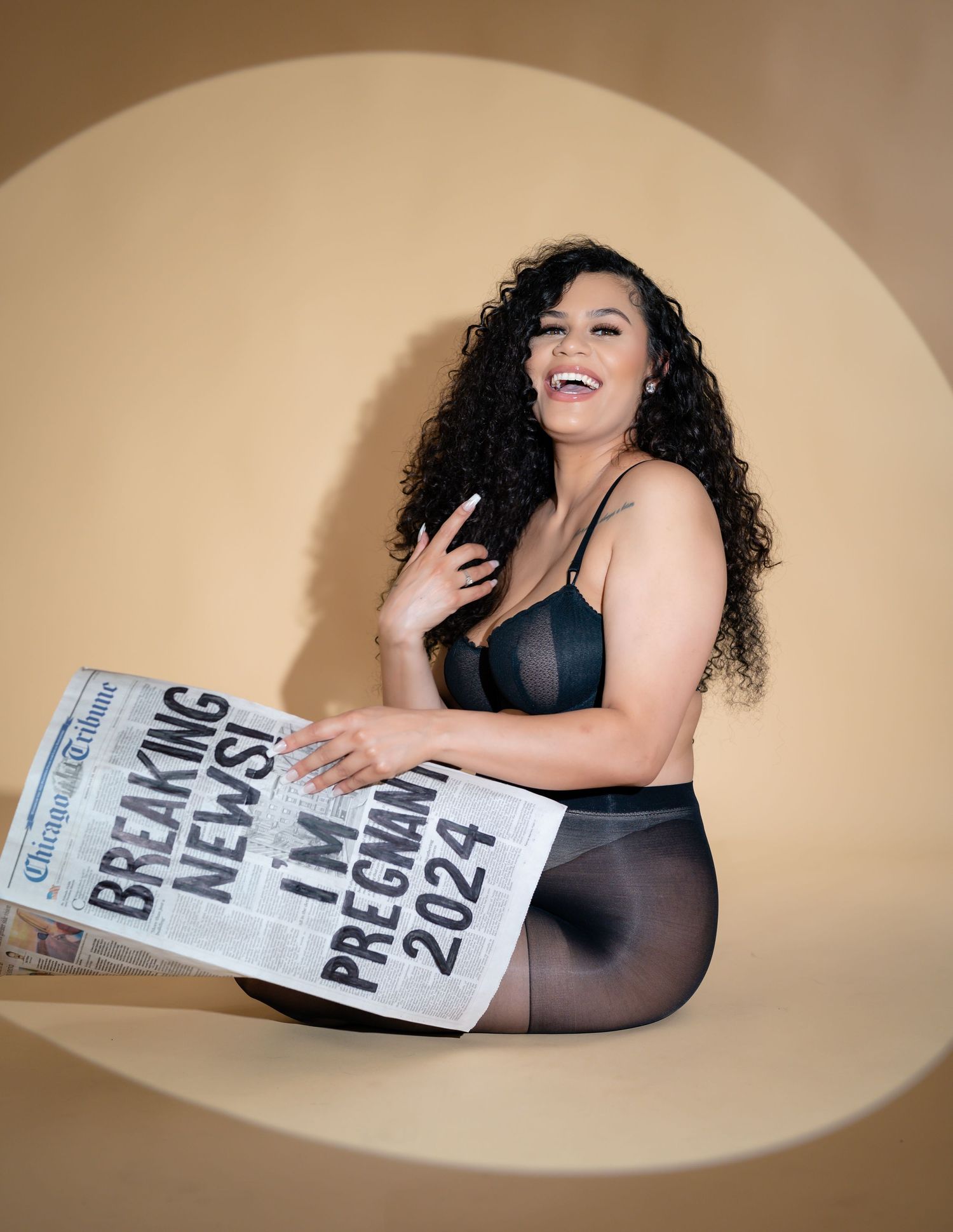 Maternity boudoir photo session with newspaper prop in warm tones.