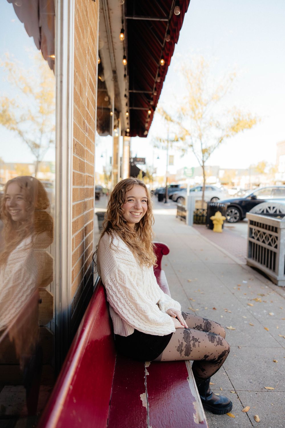 Young woman in a cream sweater sitting on a red bench outdoors on an autumn day.