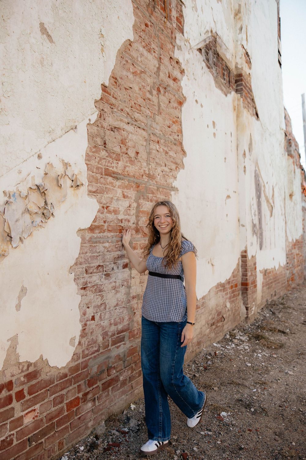 Fashion portrait series against weathered brick wall showing casual style in gingham top and jeans.