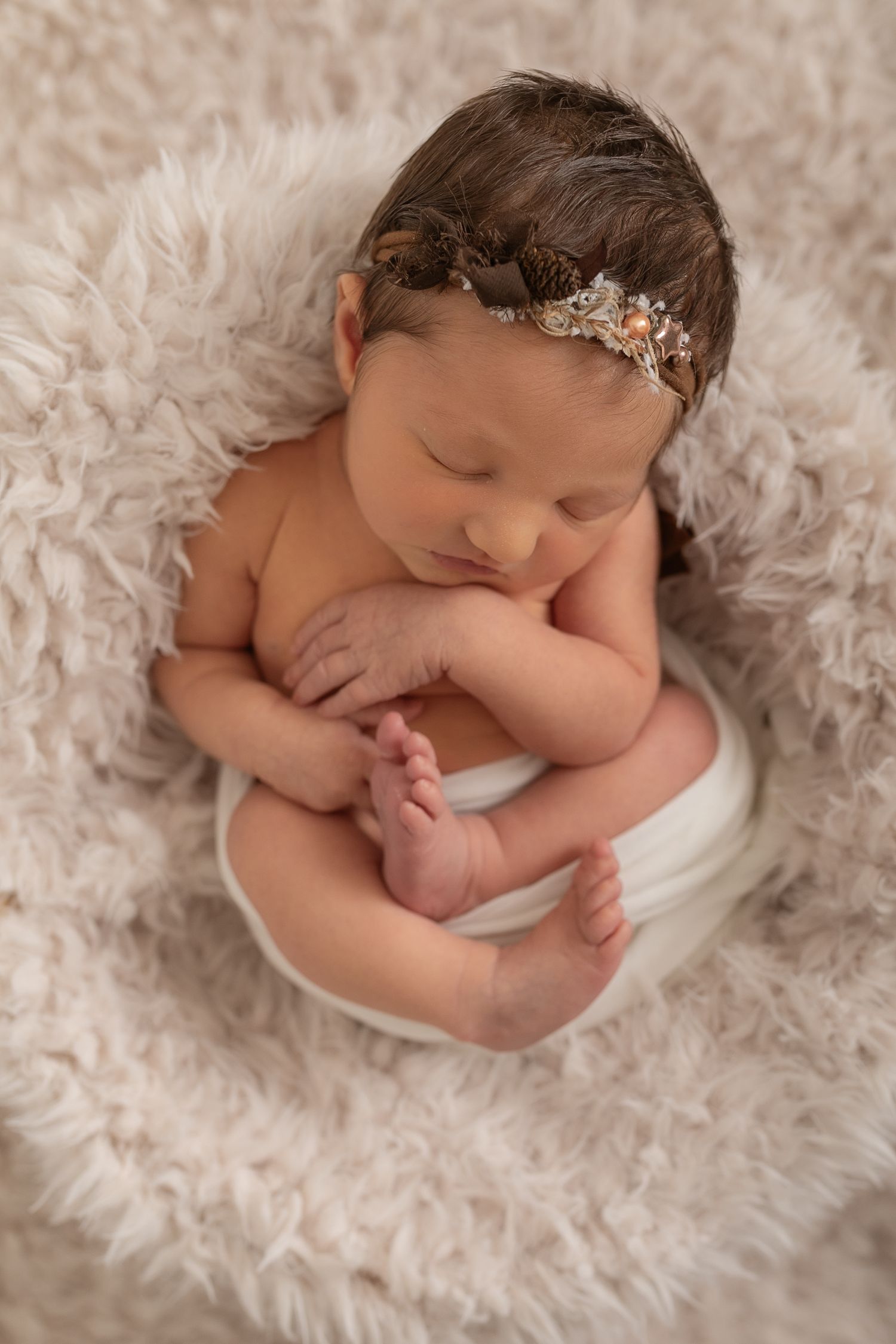 Sleeping newborn with ornate headband curled up on white fluffy backdrop. Photographer. Hull. East Yorkshire. Photography