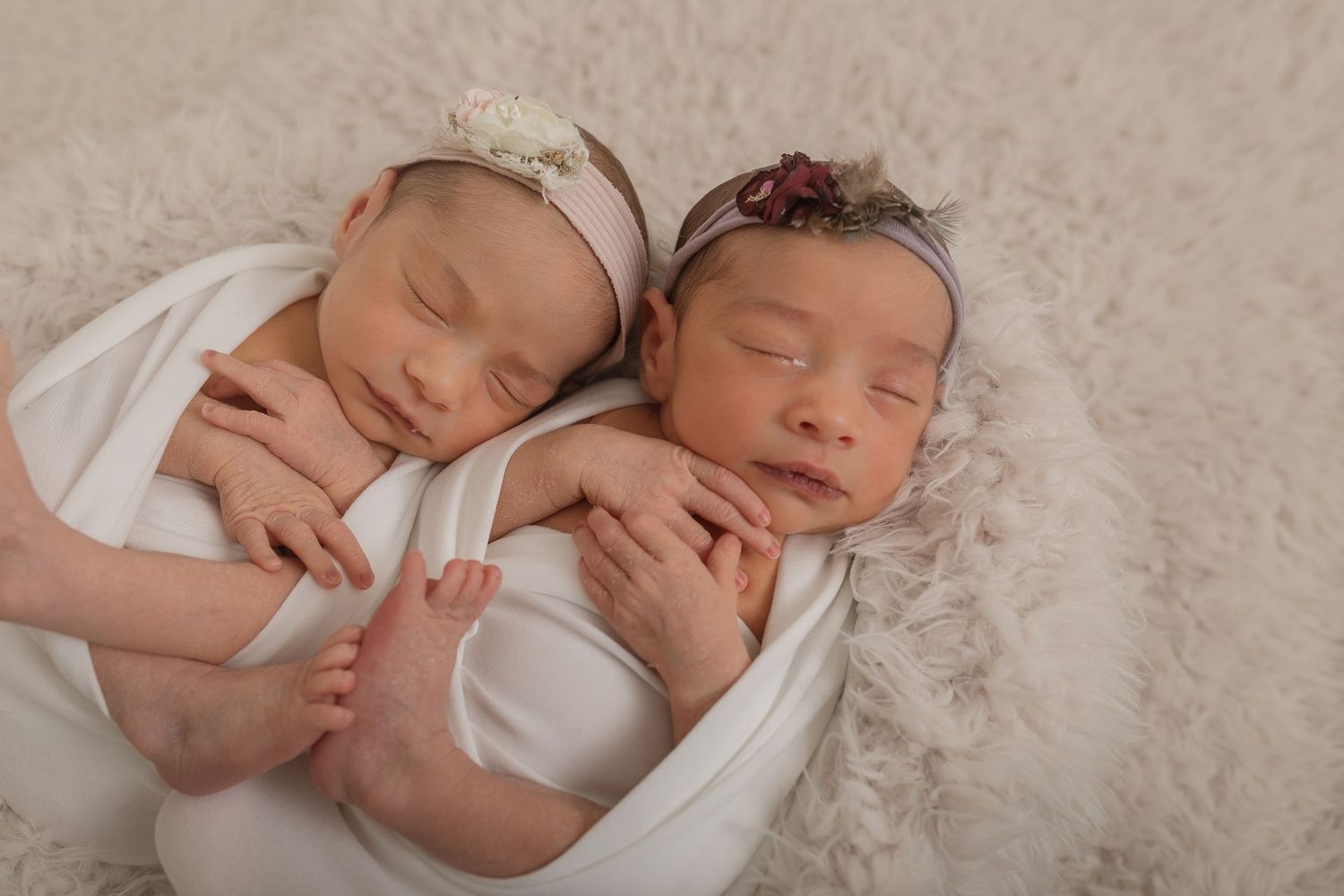 Two sleeping newborn babies wrapped in white swaddles lying together on soft cream fur blanket. Photographer. Hull. East Yorkshire. Photo