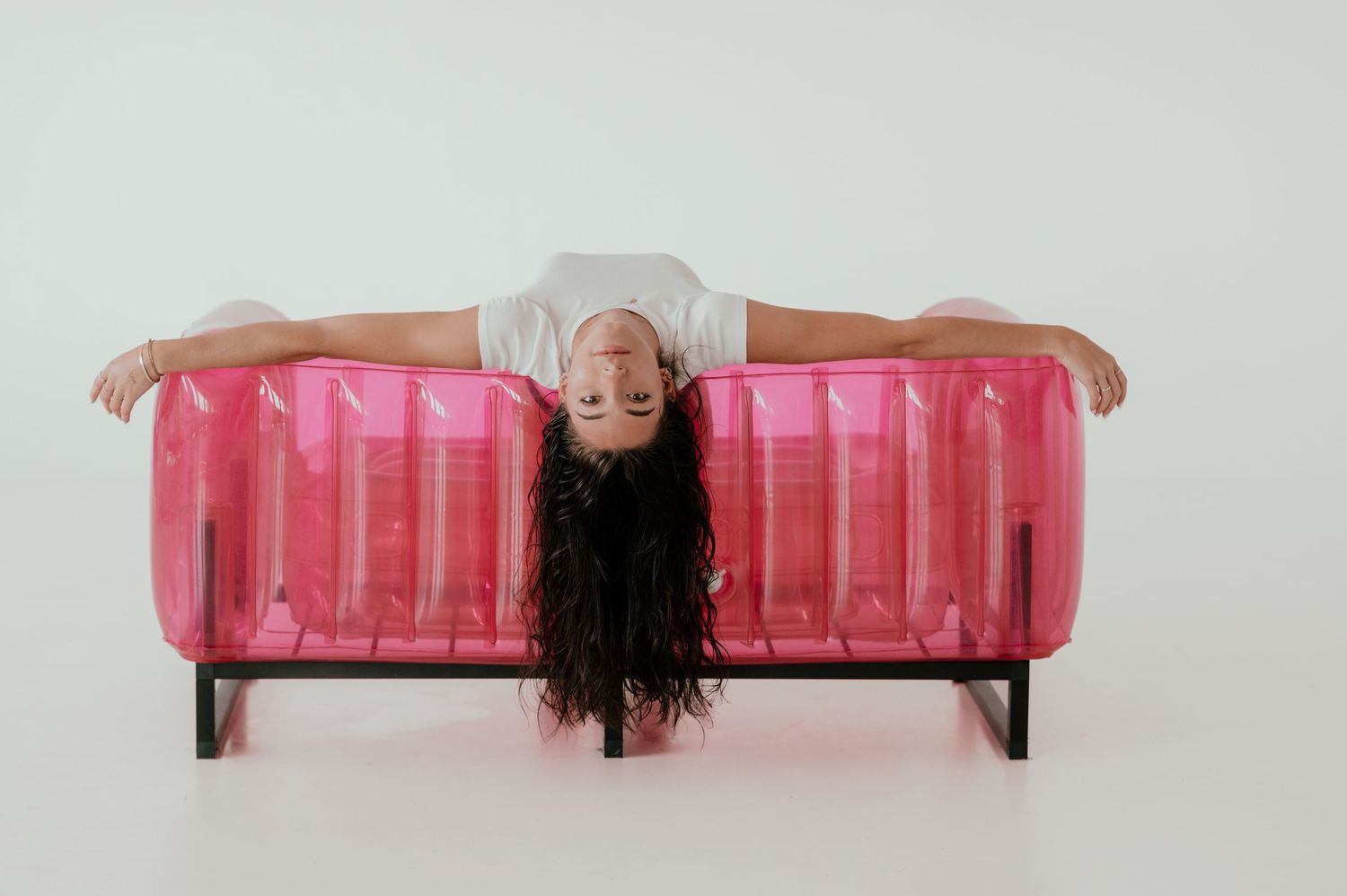 Person in white lounging upside down on a pink inflatable pool float indoors.