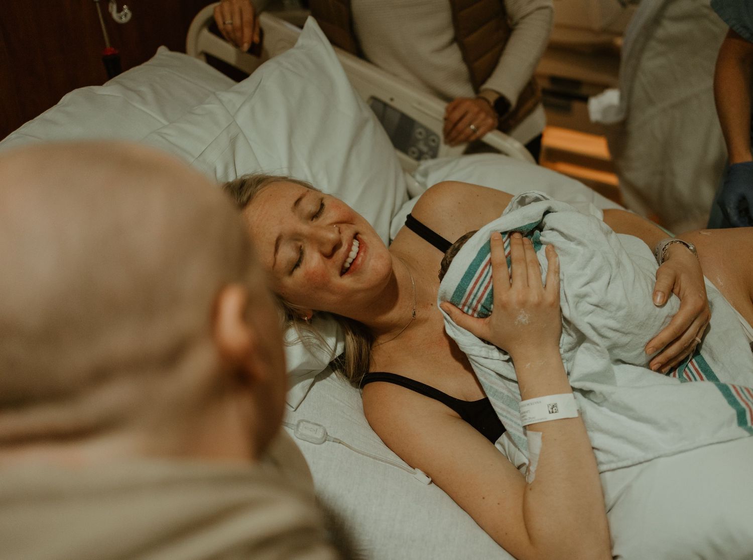 Woman lying on hospital bed smiles joyfully while receiving loving support during labor and delivery.