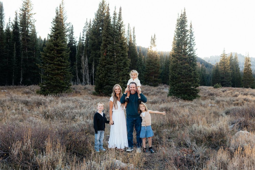 Group walks together through a scenic mountain meadow at sunset with evergreen trees in the background.