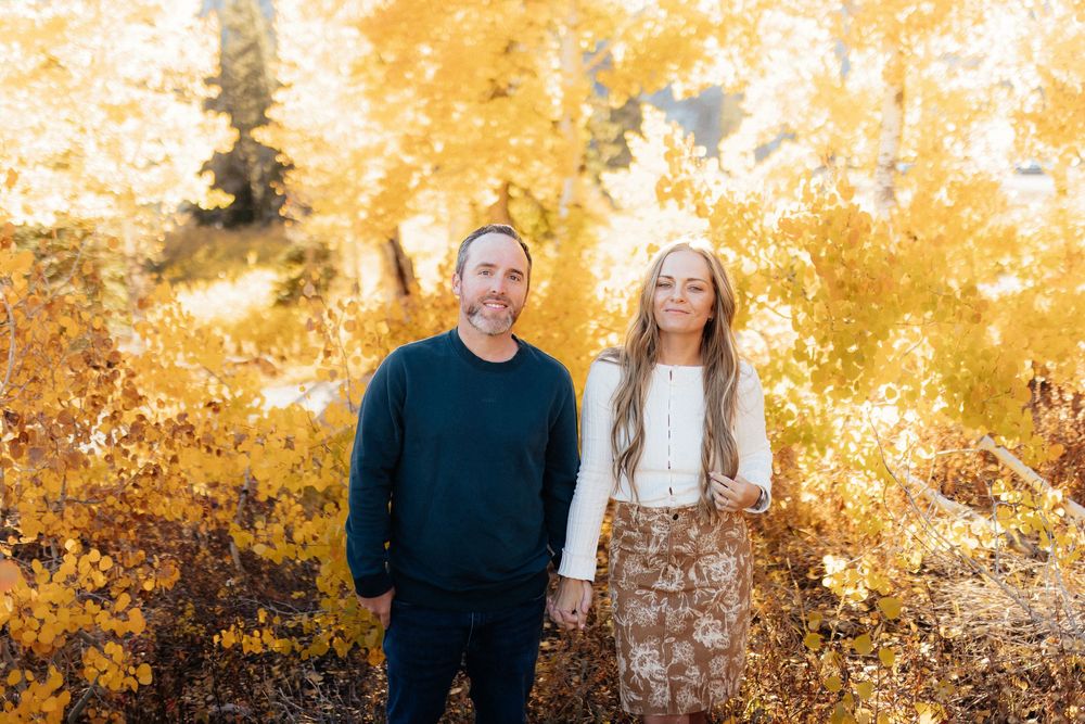 Two people pose together in front of vibrant yellow autumn foliage during a fall photo session.