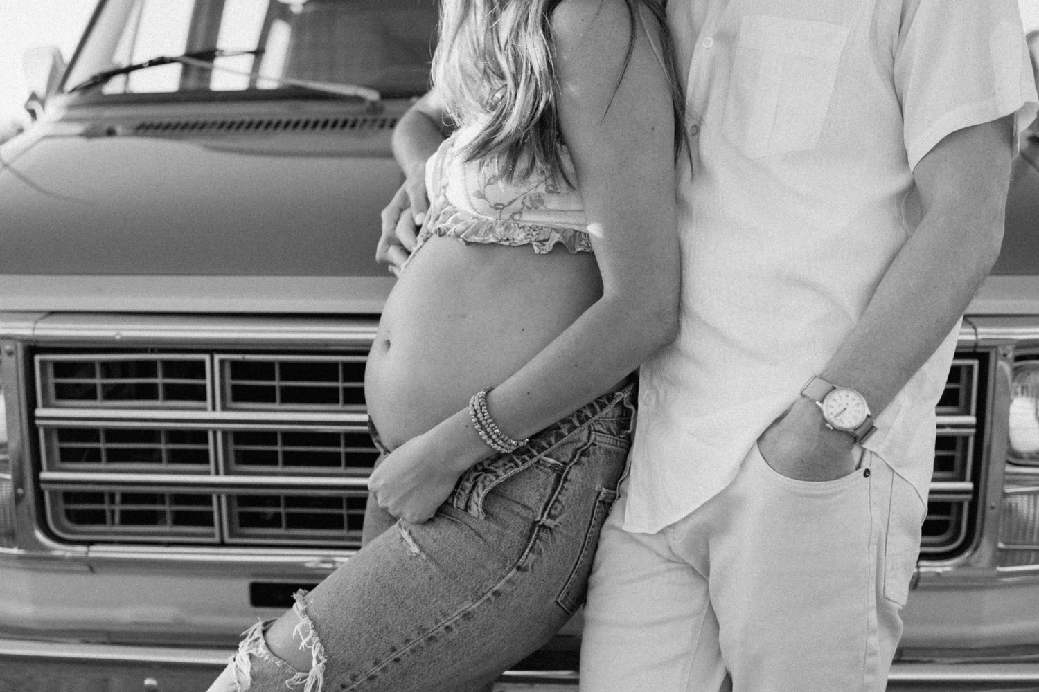 Black and white photo of expectant couple posing against vintage truck grill during maternity photoshoot in San Diego.