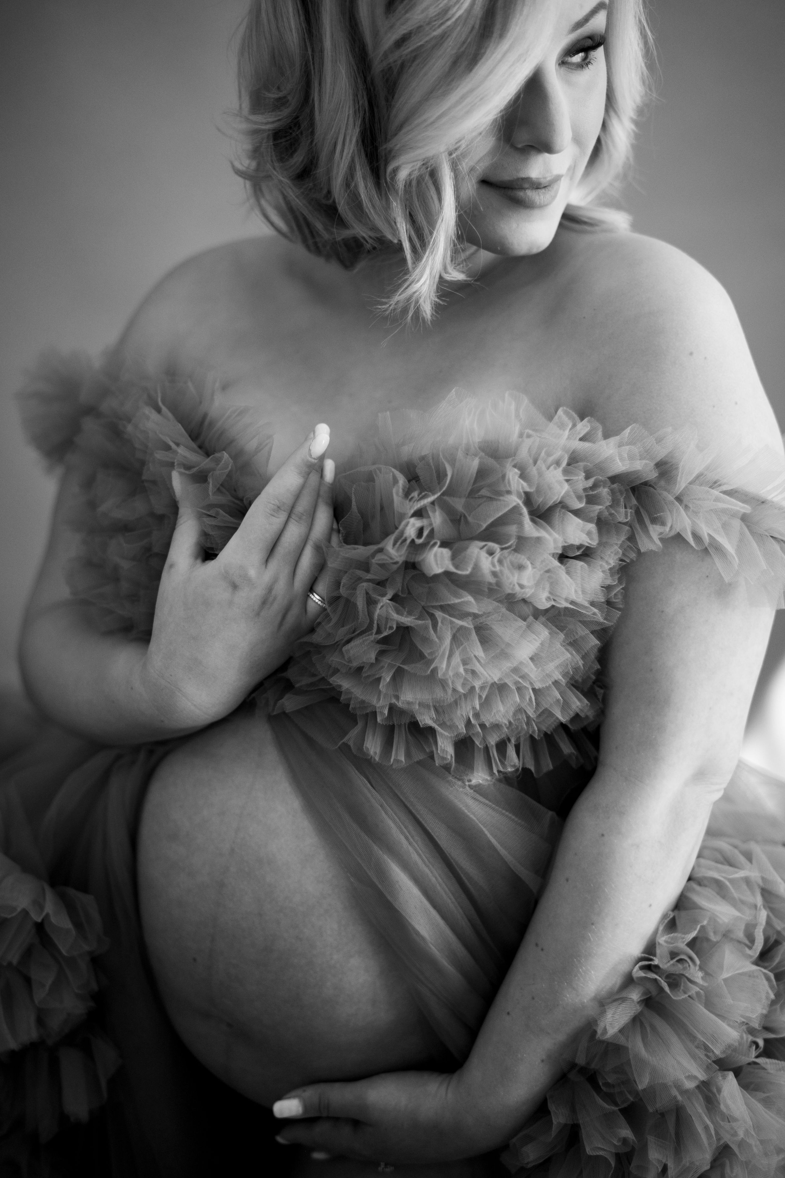 A black and white artistic maternity photo series showing a pregnant figure wearing delicate ruffled fabric.