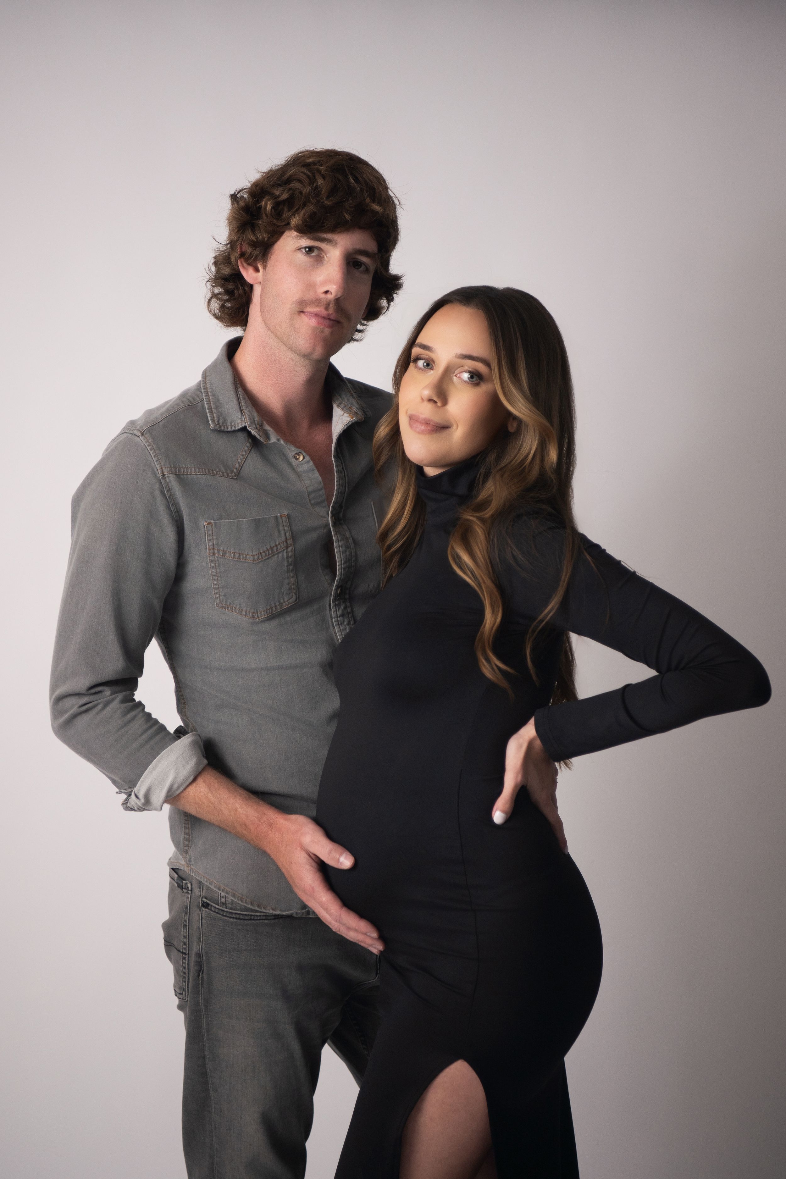 A couple in gray and black outfits pose together in a series of intimate studio portraits against a light background.