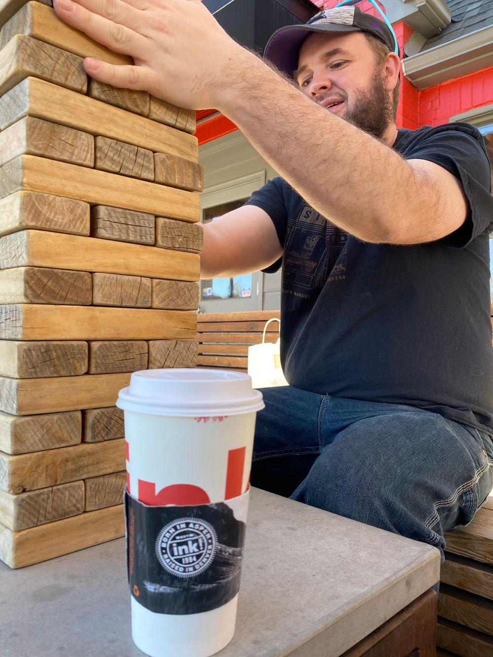 Giant Jenga game setup on outdoor patio with coffee cup.