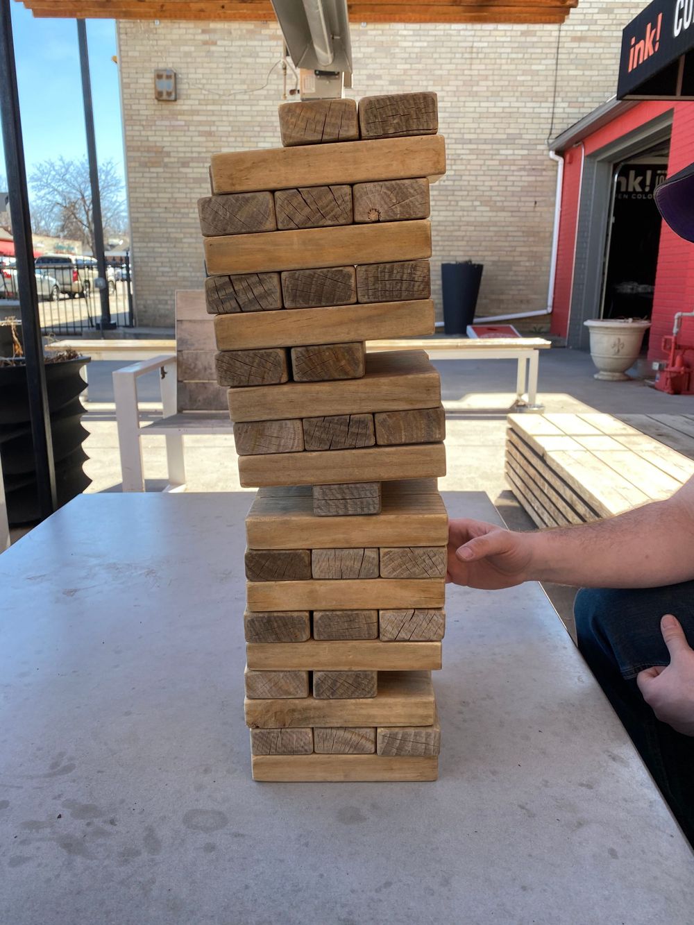 Close-up of precariously stacked wooden Jenga blocks on outdoor table.