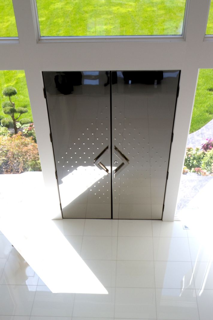 Minimalist black glass doors reflecting sunlight on white tiled floor.