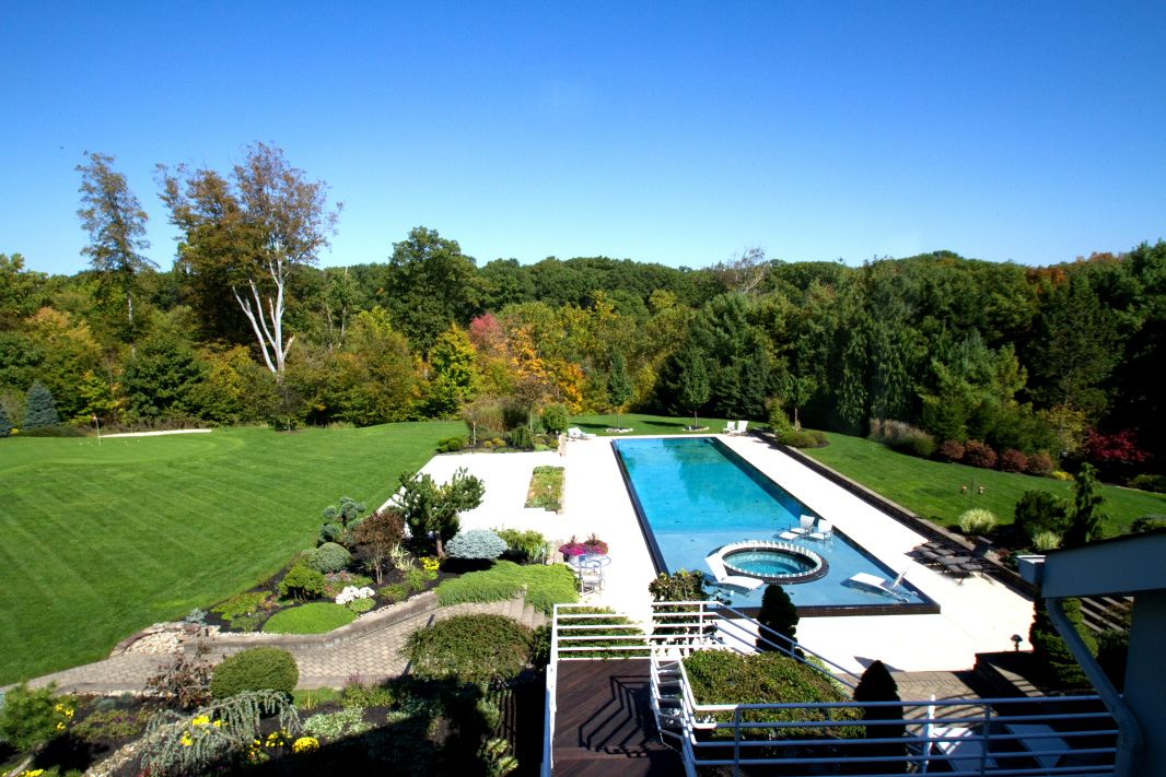 Luxury swimming pool and patio area surrounded by lush landscaping and autumn trees.