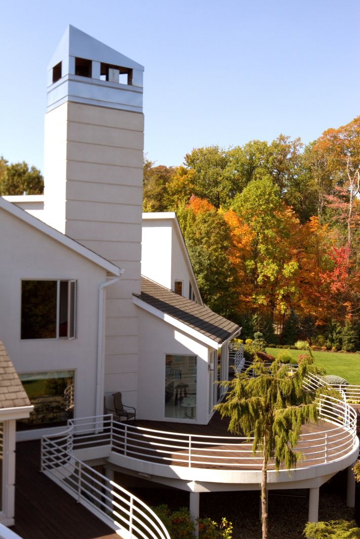 Modern white house with tall tower feature and curved deck railings amid fall foliage.