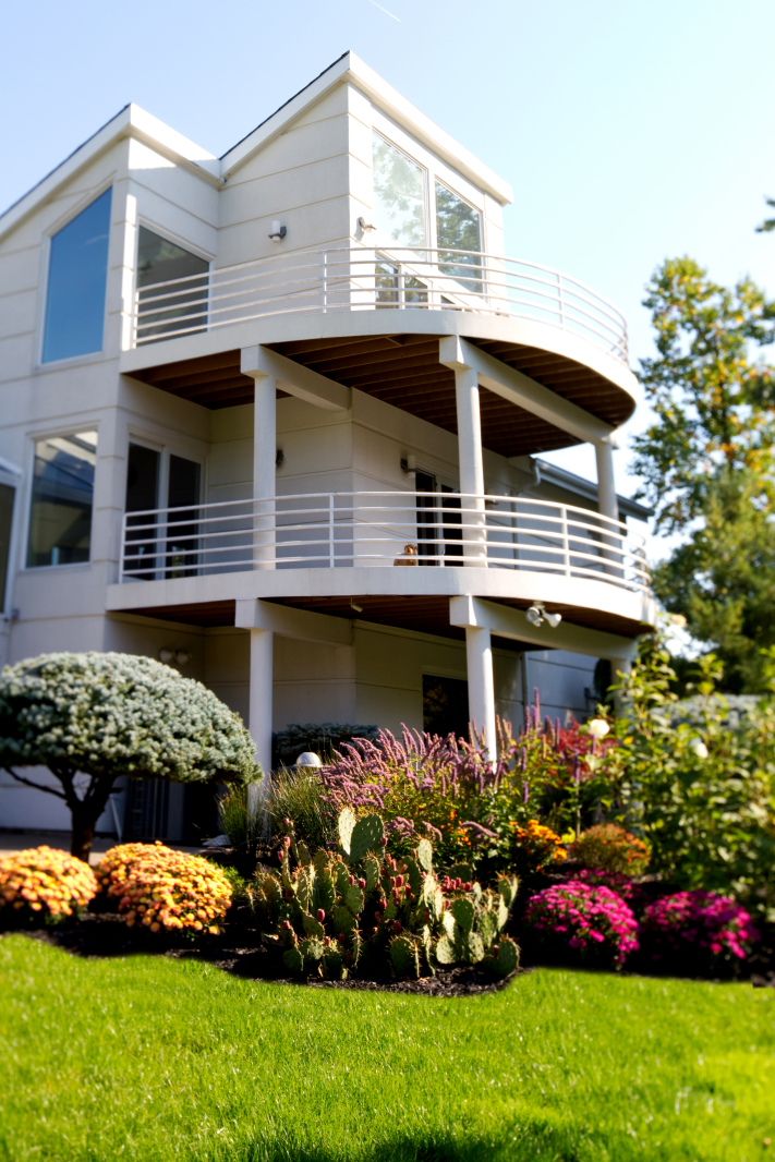 Contemporary white house with curved wraparound decks and colorful garden landscaping.