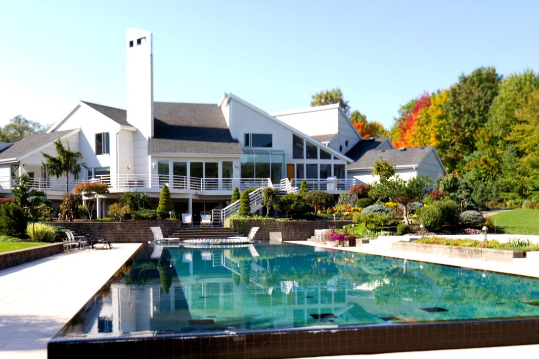 Luxury modern home with infinity pool and architectural details against autumn landscape.